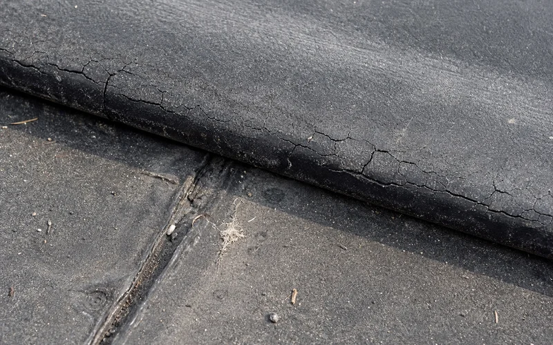 Close-up of brittle EPDM membrane edge showing age cracking
